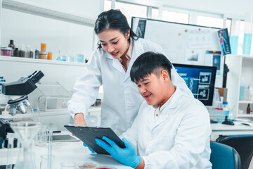 Female senior scientist supervising young male researcher in a modern lab. She reviews data on a...