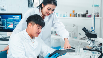 Female senior scientist supervising young male researcher in a modern lab. She reviews data on a...