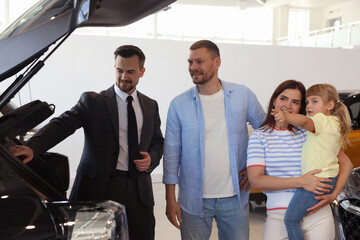 Salesman showing new car to happy family in salon