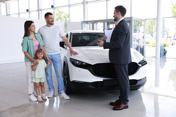 Salesman with clipboard showing new car to happy family in salon