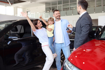 Salesman giving car key to happy family in salon