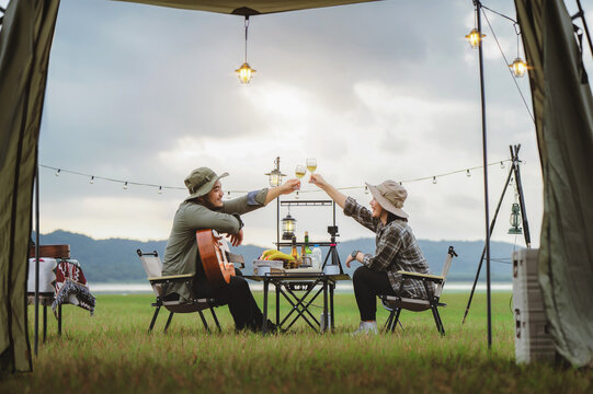 Romantic couple toasting wine near camping tent, Cheers to love under string lights and open sky nature, enjoying private camping moment. Scenic tent view of romantic outdoor picnic - Powered by Adobe