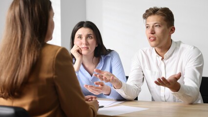 Couple complaining to woman at wooden table indoors