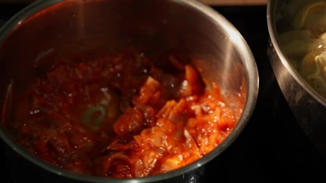 Dolly shot of tortelloni boiling beside pan with tomato sauce