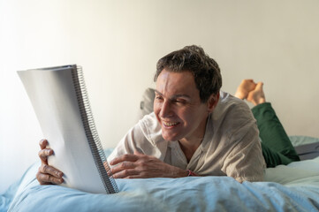 Smiling mature man lying on bed reading a notebook