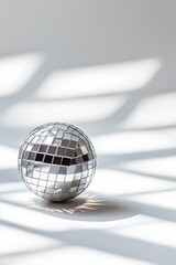 Shiny disco ball on white background, illuminated by natural light, creating dynamic shadows