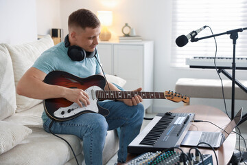 Obraz premium Man working with guitar and MIDI keyboard on sofa in home studio