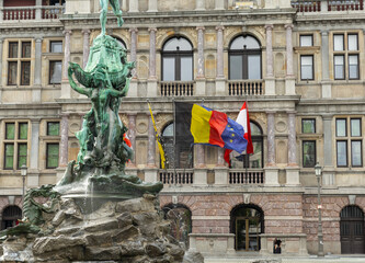 The Brabo Fountain with the Belgium, European union, Antwerp flagsflying on the city hall in...