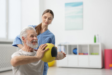 Fototapeta premium Doctor and patient exercising with medicine ball in clinic, space for text