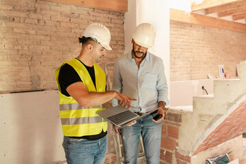 Contractor and engineer using laptop discussing project details during building construction