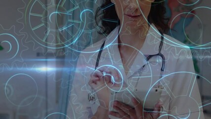 Female doctor tapping tablet and swiping data for processing while holographic cogs rotate fading - Powered by Adobe