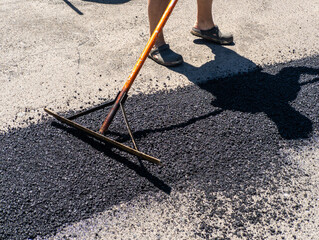 A man is using a rake to clean the asphalt of a parking lot
