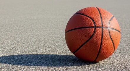 Single basketball on asphalt court surface with minimalist background perfect for sports marketing materials and advertising design.