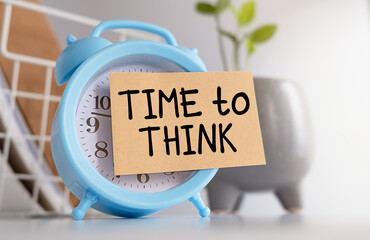 A blue alarm clock with a white face and a piece of paper with the words Time to Think written on it