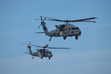 Two military Blackhawk helicopters flying in formation on clear blue sky. 