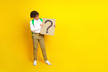 Portrait of a schoolboy holding a question mark sign against a yellow background to symbolize curiosity and learning