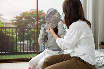 A girl in fencing gear with their mother preparing food and sports equipment