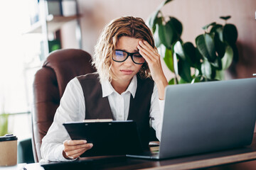 Concerned Businesswoman in Formal Attire Working at Office Desk with Laptop, Analyzing Documents,...