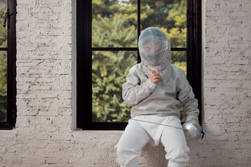 Before the tournament day, a boy dressed in fencing gear are rehearsing in gym