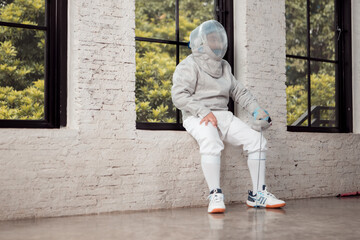 Before the tournament day, a boy dressed in fencing gear are rehearsing in gym