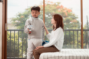 A boy in fencing gear with their mother preparing food and sports equipment