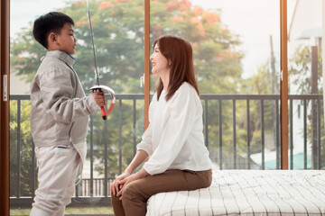 A boy in fencing gear with their mother preparing food and sports equipment