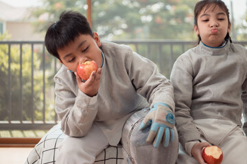 A girl and boy in fencing gear resting before practicing fencing