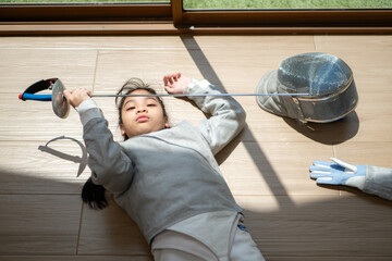 A girl in fencing gear is sitting and rest on the sidelines, exhausted from the training