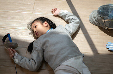 A girl in fencing gear is sitting and rest on the sidelines, exhausted from the training