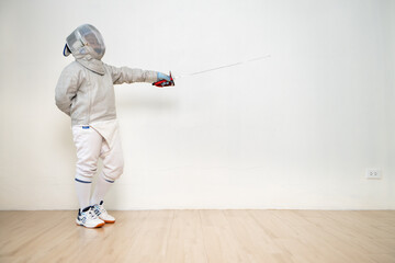 Before the tournament day, a boy dressed in fencing gear are rehearsing in gym