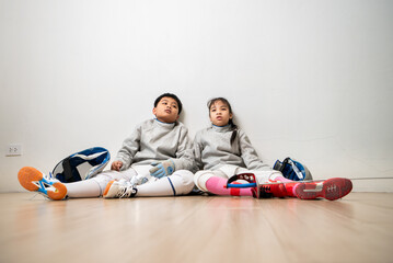 A girl and boy in fencing gear is sitting and rest on the sidelines, exhausted from the training...