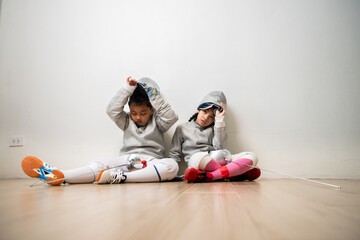 A girl and boy in fencing gear is sitting and rest on the sidelines, exhausted from the training...
