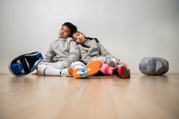 A girl and boy in fencing gear is sitting and rest on the sidelines, exhausted from the training...