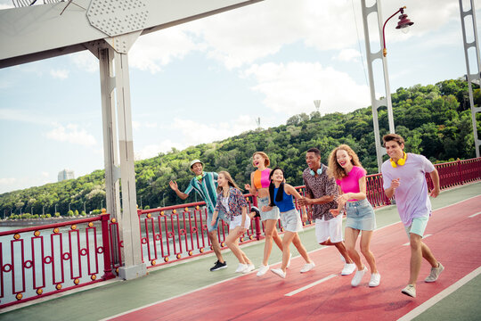 Group of diverse young friends walking on a sunny day over a bridge, enjoying leisure time and casual bonding outdoors