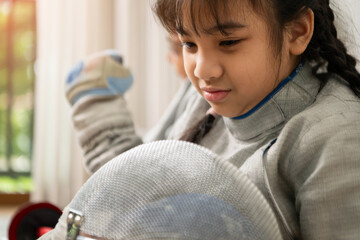 A girl in fencing gear is sitting on the sidelines, feeling disappoint for the unsuccessful game