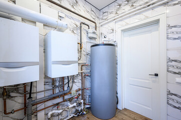 utility room with water heaters, copper piping, and a grey storage tank. The walls are tiled in a...