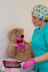 Veterinarian holding surgical scissors and showing them to teddy bear patient wearing protective...