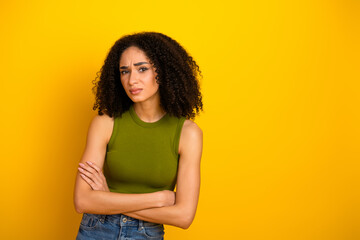Obraz premium Portrait of a young woman in a casual outfit on a yellow background, expressing emotion with her arms crossed