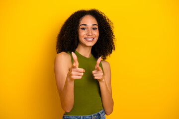 Cheerful young woman pointing with a radiant smile against a vibrant yellow background, emphasizing...