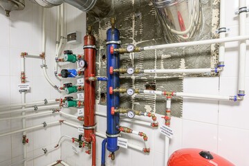 Complex plumbing system with pipes, gauges, pumps, and tanks in a tiled room, showcasing heating and water management.