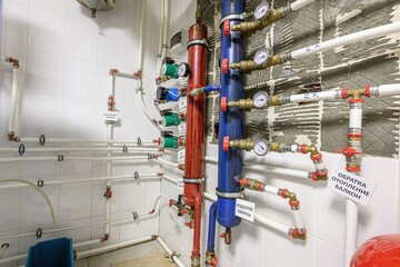 Pipes and plumbing components in a room, including red and blue tanks with gauges. Complex system with labels in a bright, tiled space