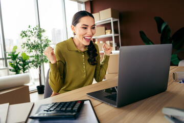 Excited female entrepreneur working in a stylish office space celebrating success on her laptop