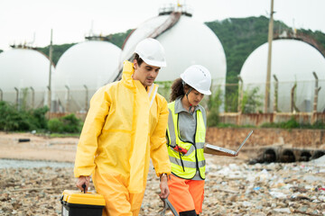 Workers in safety gear walking to survey at site near refinery storage tanks, industry facility,...