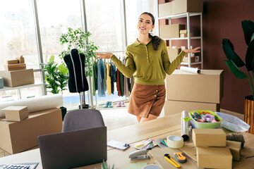 Young female entrepreneur in fashion atelier workspace surrounded by design materials showcasing...