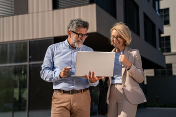 Successful Mature Businessman and Businesswoman with Laptop Outdoors, Happy and Confident in Beautiful Business District