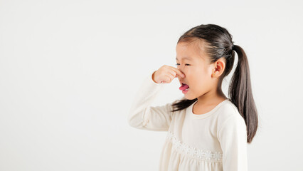 Asian young child unhappy what smell disgust expression squeezing nose with fingers. Kid girl kindergarten have something stinks bad smell situation, studio shot isolated on white background