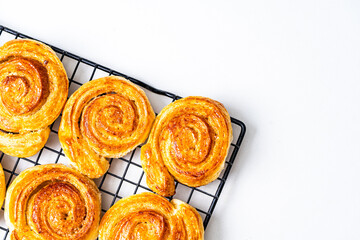 Puff pastry buns, rolls or snails with sugar and cinnamon on a black wire rack on a white background. Copyspace