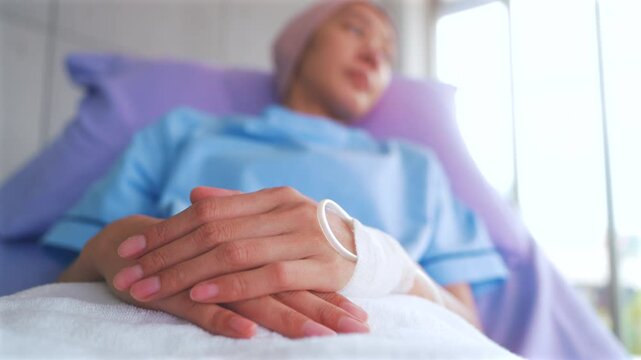 Close up of asian woman hand of a patient with patient lying on a hospital bed receiving saline in hospital ward, health and medical care concept.