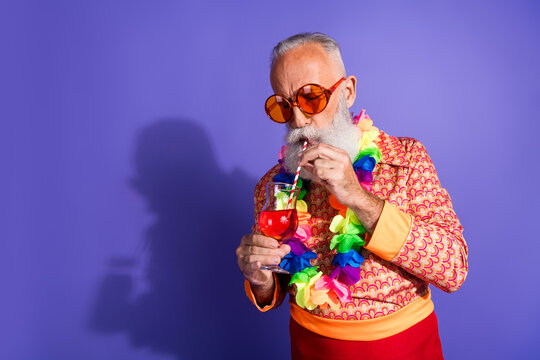 Charismatic senior man in a retro-inspired outfit sipping a cocktail while celebrating against a vibrant purple background - Powered by Adobe