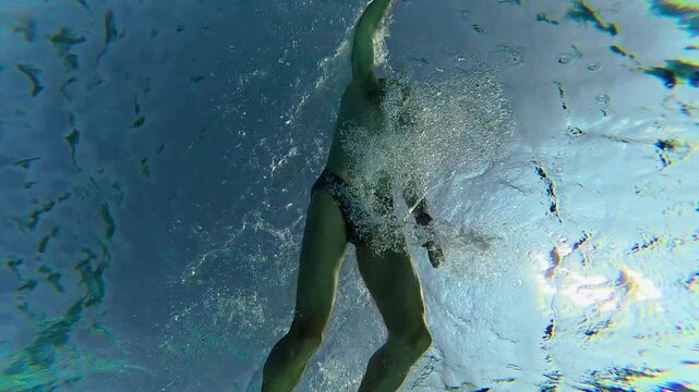 man swimming in pool, view from bottom up. Outdoor pool illuminated by sunlight